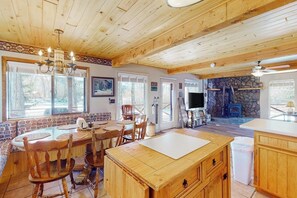 A wooden interior with a dining area, kitchen, stone wall, and a fireplace. - Charming riverfront cabin with mountain view, firepit, washer/dryer & grill (South Fork)