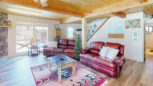 Ein großzügiges Wohnzimmer mit Holzbalkendecke, Ledersofas, einem Couchtisch und einem Weihnachtsbaum.