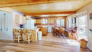 Eine geräumige Küche mit Holzausstattung, ein Essbereich mit Korbstühlen und große Fenster.