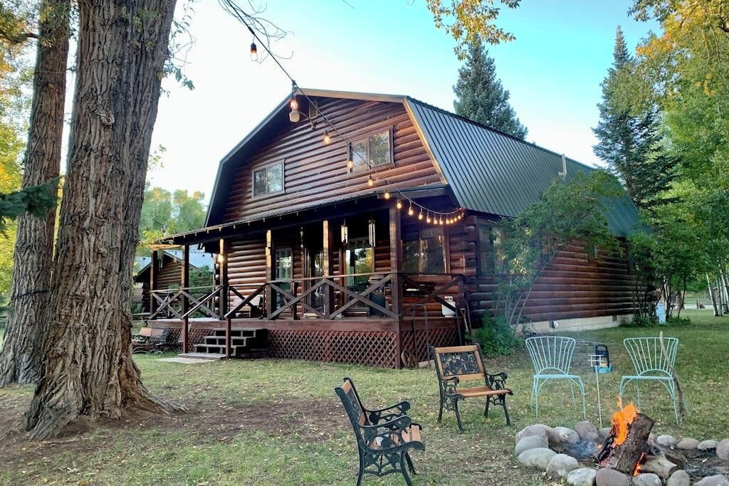 A rustic log cabin with a porch, outdoor seating, and a fire pit.