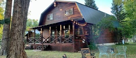 A rustic log cabin with a porch, outdoor seating, and a fire pit.
