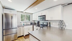 Une cuisine moderne dotée d’appareils électroménagers en acier inoxydable, de meubles blancs et d’une grande fenêtre.