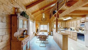 Interior de uma cabana de madeira com sala de jantar, cozinha e uma janela grande.