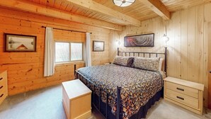 Quarto com painéis de madeira, uma cama, mesas de cabeceira, janela com cortinas e luminária no teto.