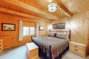 Ein Schlafzimmer mit Holzwandverkleidung, einem Bett, Nachttischen, einem Fenster mit Vorhängen und einer Deckenleuchte.