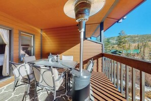 A balcony with a table and chairs, a heater, and a view of a forested area. - Peaceful condo with balcony, loft, shared sauna, & fireplace (Frisco)