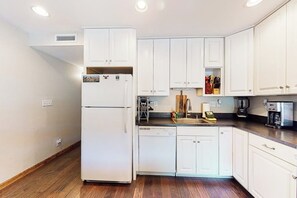A kitchen with white cabinets, a refrigerator, a dishwasher, and a coffee maker. - Peaceful condo with balcony, loft, shared sauna, & fireplace (Frisco)