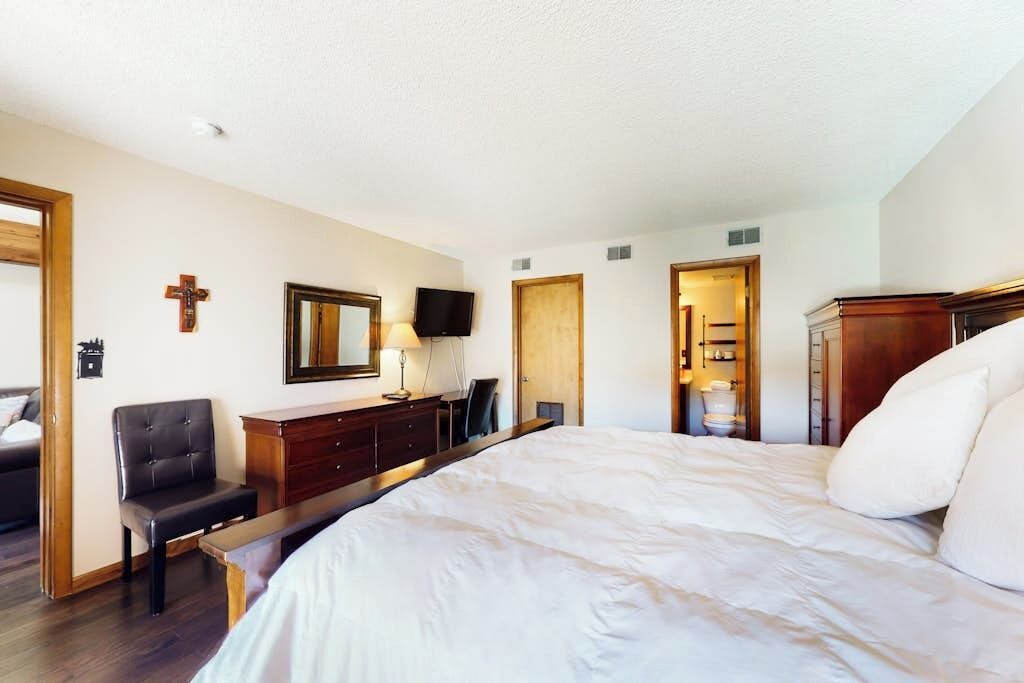 Habitación de hotel con una cama grande, un escritorio con silla, televisión, una cruz en la pared y un armario de madera.