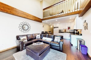A spacious living area with a leather sectional sofa, a coffee table, and a staircase leading to an upper level. - Peaceful condo with balcony, loft, shared sauna, & fireplace (Frisco)