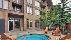Une piscine entourée de chaises en bois, un bâtiment doté de nombreux balcons et un arbre.