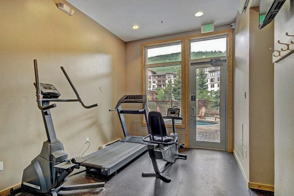 A gym with treadmills and exercise equipment, a door leading to a balcony with a view of buildings and greenery.