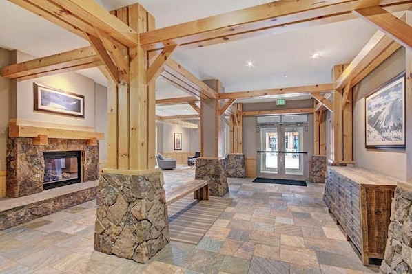Eine großzügige Lobby mit Kamin aus Stein, Holzbalken und einer Steinsitzbank.