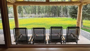 Un espace extérieur abrité, aménagé avec des sièges, d’où l’on peut admirer une forêt et un champ de fleurs jaunes.