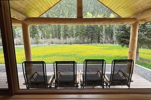 Ein überdachter Außenbereich mit Blick auf einen Wald und ein Feld voller gelber Blumen.