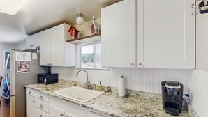 Una cucina con mobili bianchi, un piano di lavoro in granito, un lavello, un forno a microonde, una macchina da caffè e una finestra con vista.