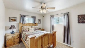 Una camera da letto con un letto in legno, una ventola a soffitto, un comodino, una lampada e una finestra con tende.