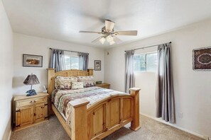 Ein Schlafzimmer mit einem hölzernen Bett, einem Deckenventilator, einem Nachttisch, einer Lampe und einem Fenster mit Vorhängen.