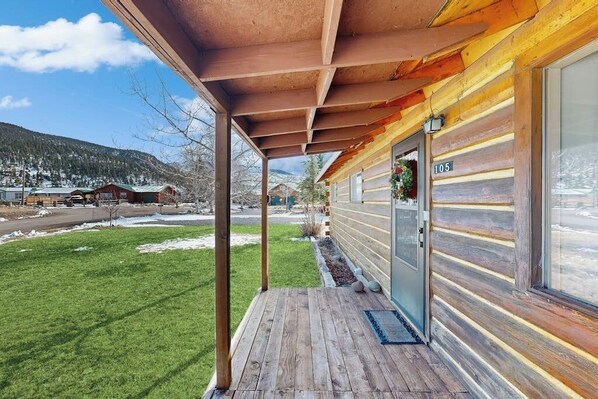 Eine Holzhütte mit Veranda, einer Tür mit Hausnummer und Blick auf eine verschneite Landschaft.
