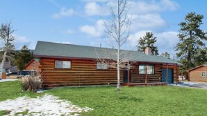 Una baita con tetto verde, un portico e un piccolo giardino con erba e un albero.