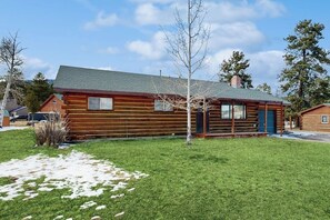 Eine Blockhütte mit grüner Dachdeckung, einer Veranda und einem kleinen Garten mit Gras und einem Baum.