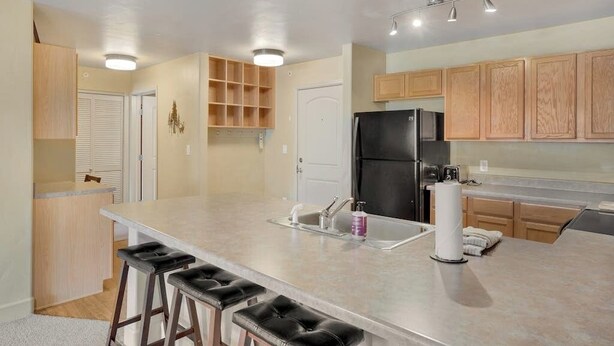 Una cocina moderna con una isla central, taburetes de bar, armarios de madera y un refrigerador negro.