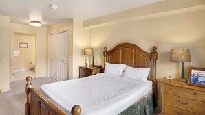 Un dormitorio con una cama de madera, mesitas de noche con lámparas, un aparador y una puerta que da a otra habitación.