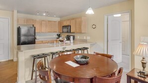 Una cocina compacta con armarios de madera, una isla central y un comedor con una mesa redonda y sillas.