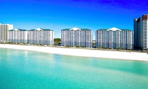 Ein Hotel direkt am Strand mit mehreren Hochhäusern, einem Sandstrand und blauem, klarem Himmel.
