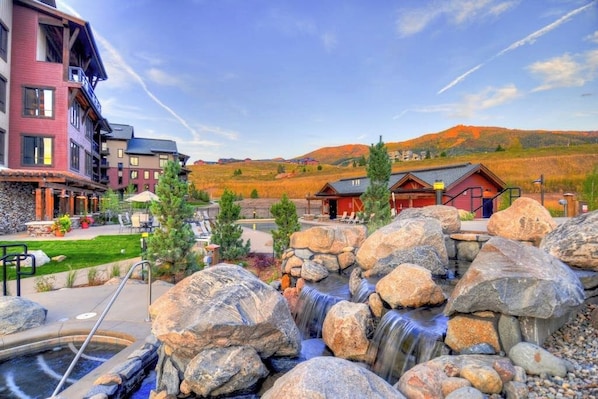 A hotel with a pool, a waterfall feature, and a view of the surrounding hills. - Condo with two balconies, fireplace, on-site gondola, pool & three hot tubs (Steamboat Springs)