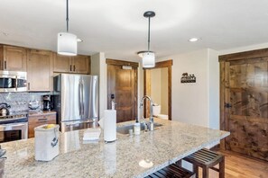 A kitchen with granite countertops, stainless steel appliances, wooden cabinets, and a 'WELCOME' sign. - Condo with two balconies, fireplace, on-site gondola, pool & three hot tubs (Steamboat Springs)