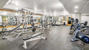 Un gimnasio con equipos de ejercicio variados, un espejo y un reloj de pared.