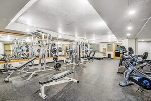 Ein Fitnessraum mit verschiedenen Trainingsgeräten, einem Spiegel und einer Wanduhr.