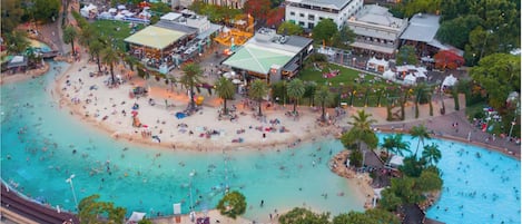 Vista aérea de uma área costeira com praia, piscina e edifícios ao redor.