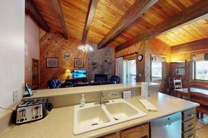 A kitchen with a double sink, wooden ceiling beams, a stone accent wall, and a television in the background. - Steamboat Springs condo with pool, hot tub, fitness center & fireplace (Steamboat Springs)