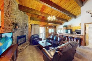 A rustic interior with stone walls, wooden beams, leather furniture, a fireplace, and a television. - Steamboat Springs condo with pool, hot tub, fitness center & fireplace (Steamboat Springs)