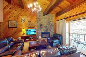 A wooden-paneled room with leather sofas, a fireplace, a television, and a balcony with outdoor furniture. - Steamboat Springs condo with pool, hot tub, fitness center & fireplace (Steamboat Springs)