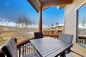 Eine Holzterrasse mit Tisch und Stühlen, mit Blick auf eine verschneite Landschaft und Gebäude.