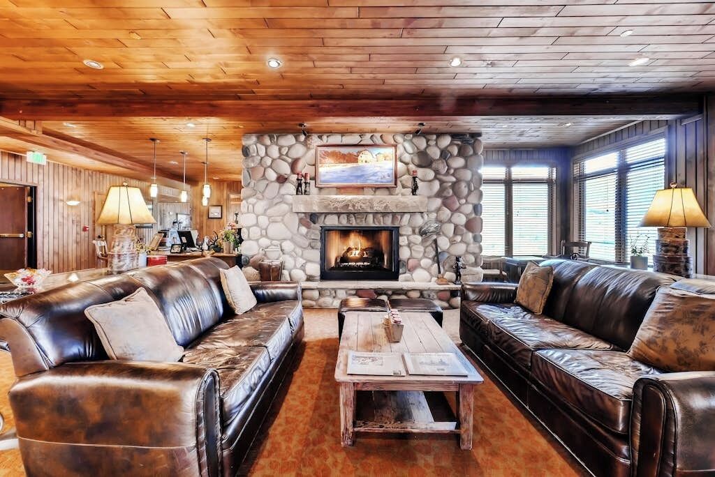 A cozy lobby with leather sofas, a stone fireplace, and a wooden ceiling.