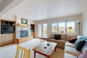 A living room with a fireplace, a sofa, a TV, and a dining table. - Luxury home one block from gondola w/mountain views, free WiFi, & private W/D (Steamboat Springs)