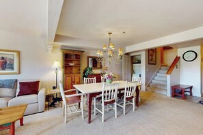 A dining area with a chandelier, a dining table with chairs, a sofa, a lamp, and a staircase leading to another room. - Luxury home one block from gondola w/mountain views, free WiFi, & private W/D (Steamboat Springs)