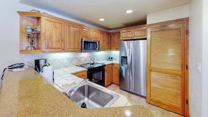 A kitchen with wooden cabinets, stainless steel appliances, and a tiled backsplash. - EagleRidge Lodge 103 Bright, walk-to-lift condo w/ fireplace, W/D & shared hot tubs/pool/gym/shuttle (Steamboat Springs)