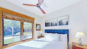 A bedroom with a bed, a ceiling fan, a nightstand, a lamp, a window with blinds, and wall art. - EagleRidge Lodge 103 Bright, walk-to-lift condo w/ fireplace, W/D & shared hot tubs/pool/gym/shuttle (Steamboat Springs)