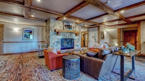 A spacious room with a stone fireplace, a sofa, a round table, and a patterned carpet. - EagleRidge Lodge 103 Bright, walk-to-lift condo w/ fireplace, W/D & shared hot tubs/pool/gym/shuttle (Steamboat Springs)