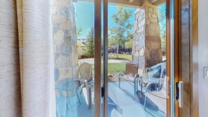 A glass door leading to an outdoor patio with stone pillars, chairs, and a table. - EagleRidge Lodge 103 Bright, walk-to-lift condo w/ fireplace, W/D & shared hot tubs/pool/gym/shuttle (Steamboat Springs)