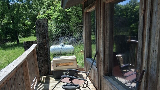 Eine Holzterrasse mit zwei Stühlen, einem Grill und Blick ins grüne Umland.