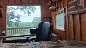 Ein Zimmer mit einem Bett, einem Schreibtisch mit Stuhl, einem Fenster mit Blick auf Bäume und einer Decke mit Himmelmotiv.