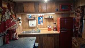 Eine kleine Küche mit Holzausbau, einem roten Kühlschrank, einer Kaffeemaschine und einem Spülbecken.