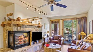 Una sala de estar con chimenea de piedra, sofás de cuero, televisor y ventilador de techo.