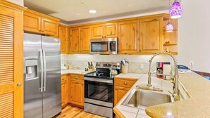 Cocina con gabinetes de madera, electrodomésticos de acero inoxidable, encimera de granito y una lámpara colgante.