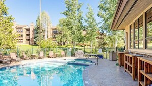Une piscine dotée de chaises longues et d’un espace bar, le tout entouré d’arbres et d’immeubles.
